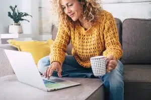 lady with blonde curly hair work at the notebook sit down on the sofa at home - check on oline shops for cyber monday sales - technology woman concept for alternative office freelance