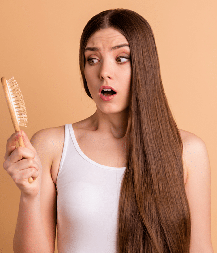 Woman with long straight hair holding a hairbrush and looking at it with a surprised face.