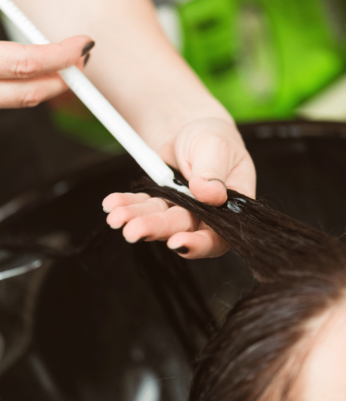 A hair professional applying a syringe of conditioner to a client's wet hair.