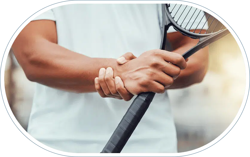 Young man holding a tennis racket in one hand and his wrist in the other.