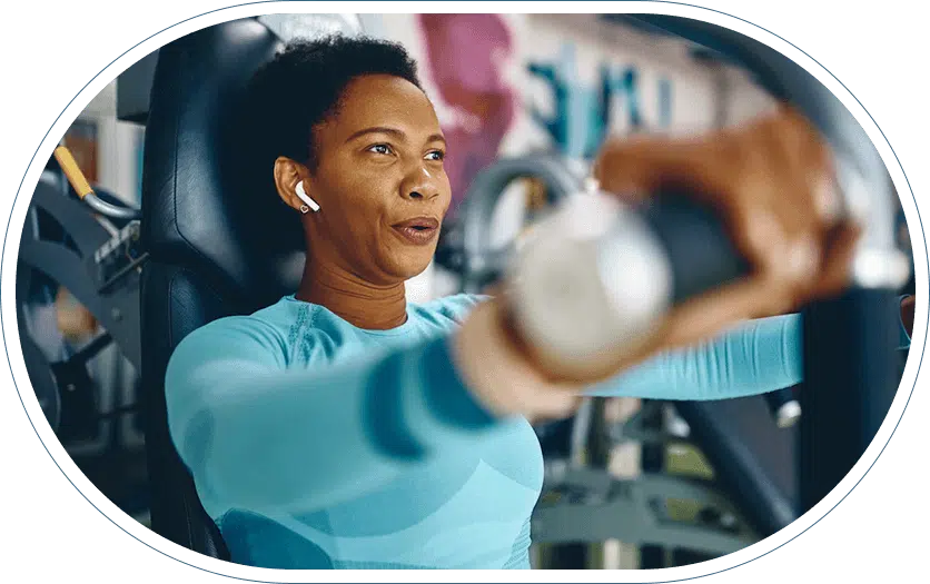 Young athletic woman at the gym wearing ear buds and using a weightlifting machine.