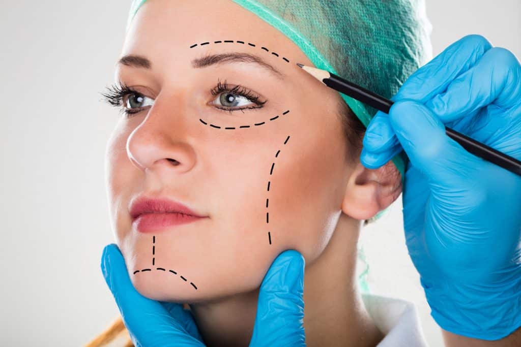 A Surgeon Drawing Perforation Lines On Young Woman's Face