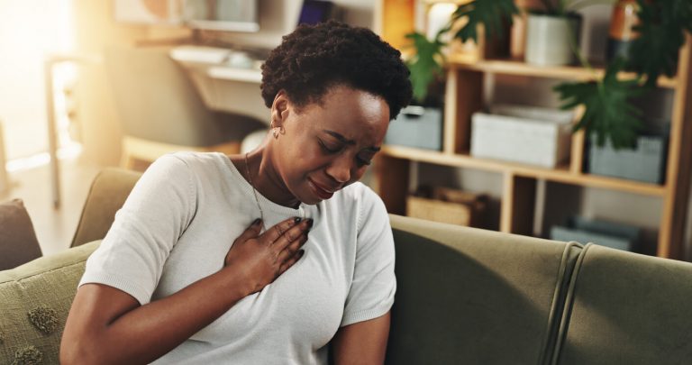Breathing, chest pain or heartburn with black woman on sofa in living room of home for discomfort.